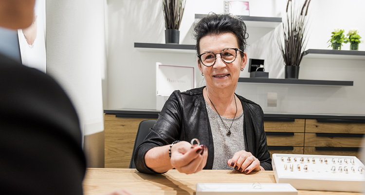 Beraterin bei Optik und Schmuck Osswald in Burgau präsentiert in einem modernen Beratungsraum einen Trauring. Freundliche persönliche Beratung mit großer Auswahl an Ringen im Hintergrund.