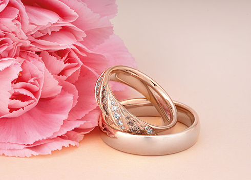 Zwei elegante Trauringe in Roségold mit Diamanten, fotografiert vor rosa Nelke – exklusive Eheringe bei Optik und Schmuck Osswald in Burgau, Süddeutschland