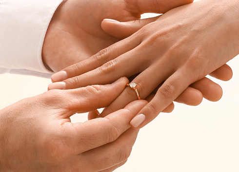 Mann steckt Frau einen eleganten Verlobungsring aus Gelbgold mit Solitär-Diamant an – erhältlich bei Optik und Schmuck Osswald in Burgau, Süddeutschland.